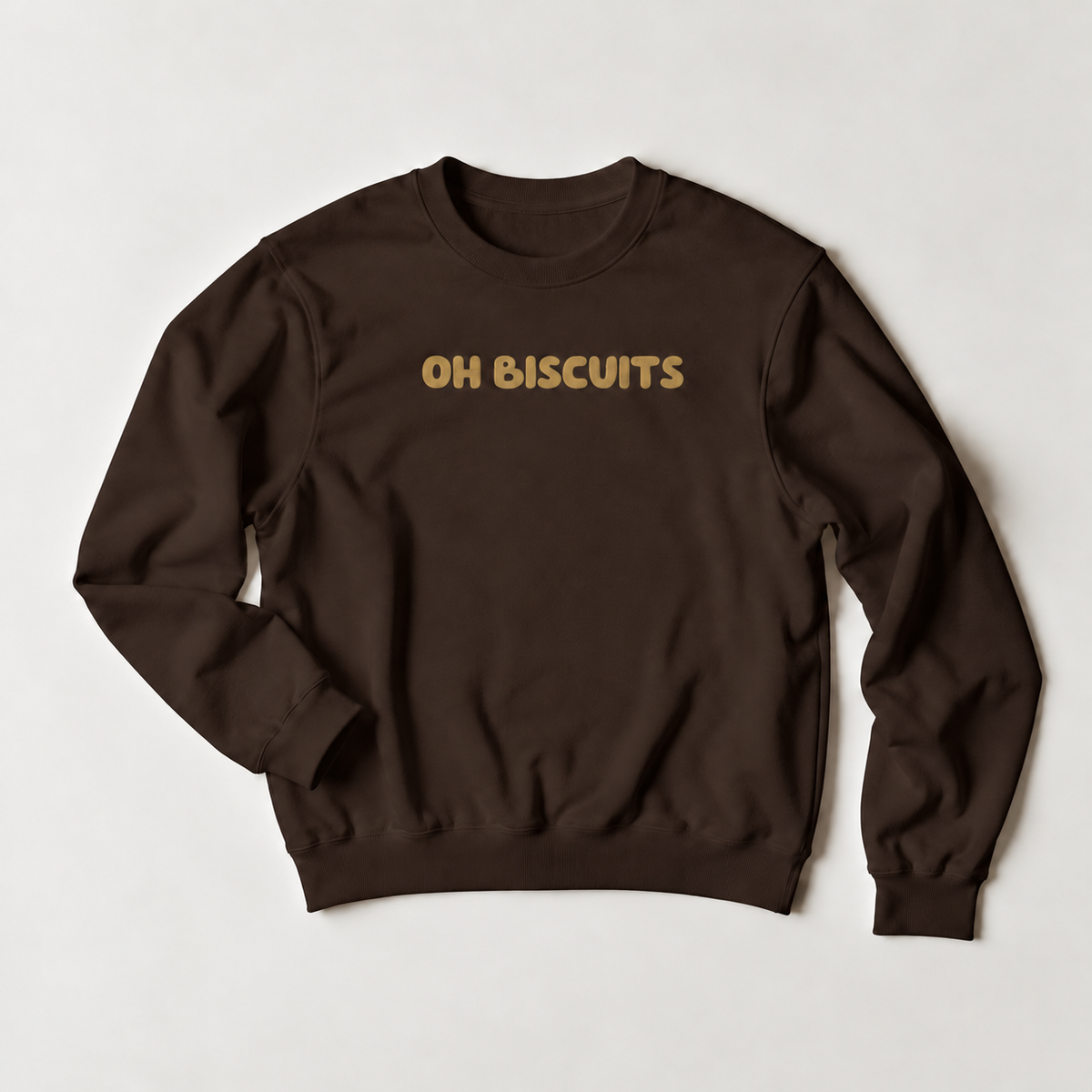 A dark brown crewneck sweatshirt with the phrase 'OH BISCUITS' printed across the chest in a gold-colored retro font, laid flat on a light gray background.